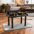 Raised dog bowl stand with two stainless steel bowls on a paw-print feeding mat in a living room